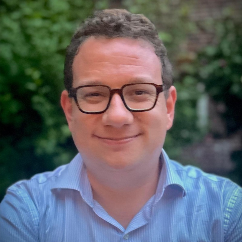 Dave Kasten, smiling, in glasses and a light blue collared shirt